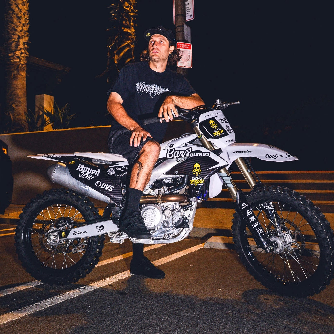 Man sitting on a dirt bike at night with palm trees in the background