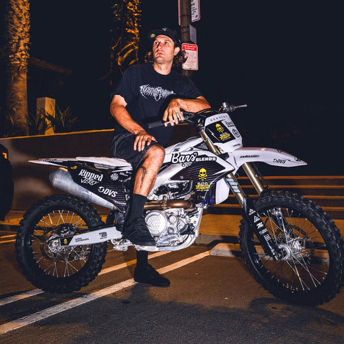 Man sitting on a dirt bike at night with palm trees in the background