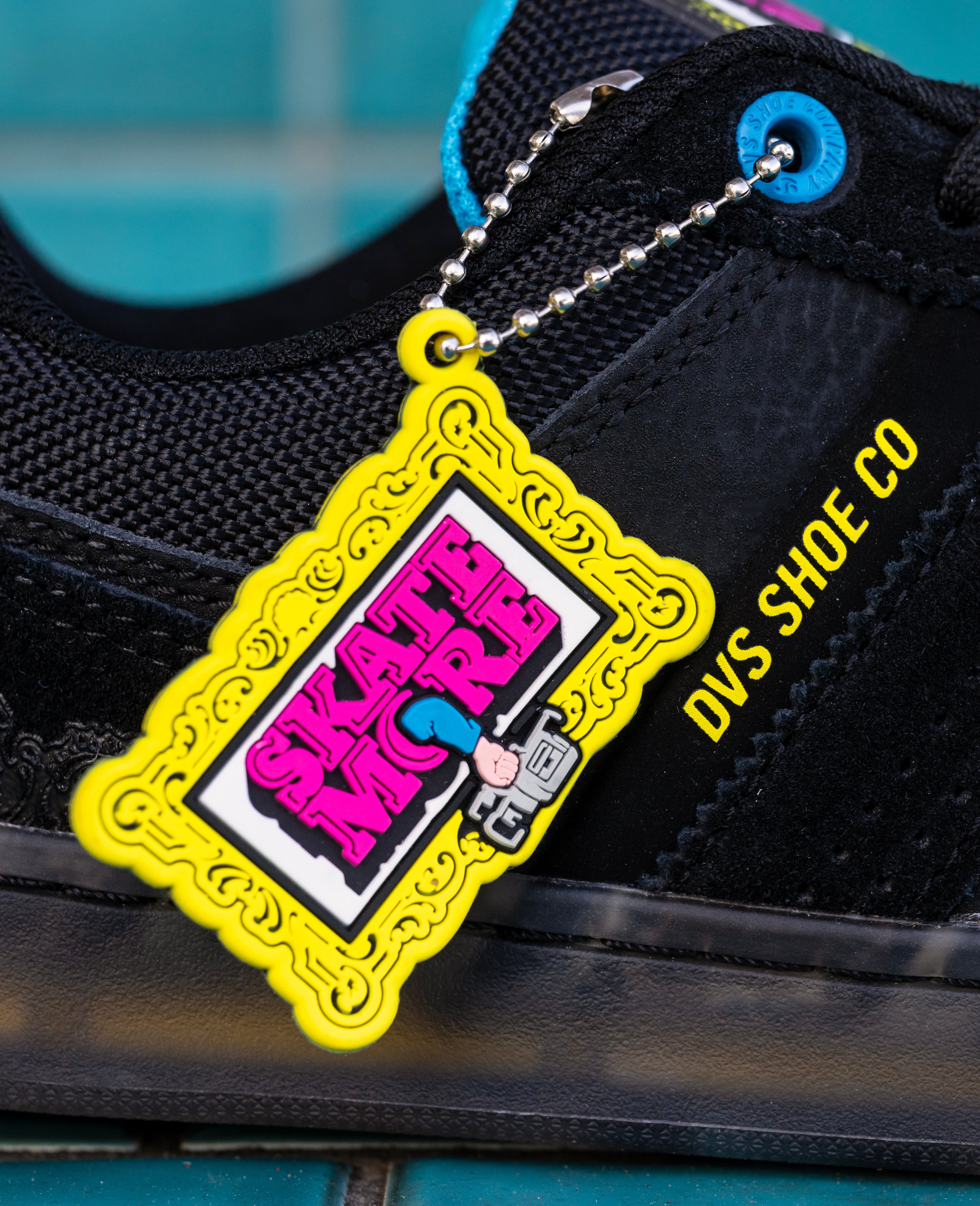 Black DVS sneaker with a colorful keychain featuring 'Skate More' branding on a blue tiled background.