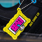 Black sneaker with a colorful keychain featuring 'Skate MC' branding on a blue tiled background.