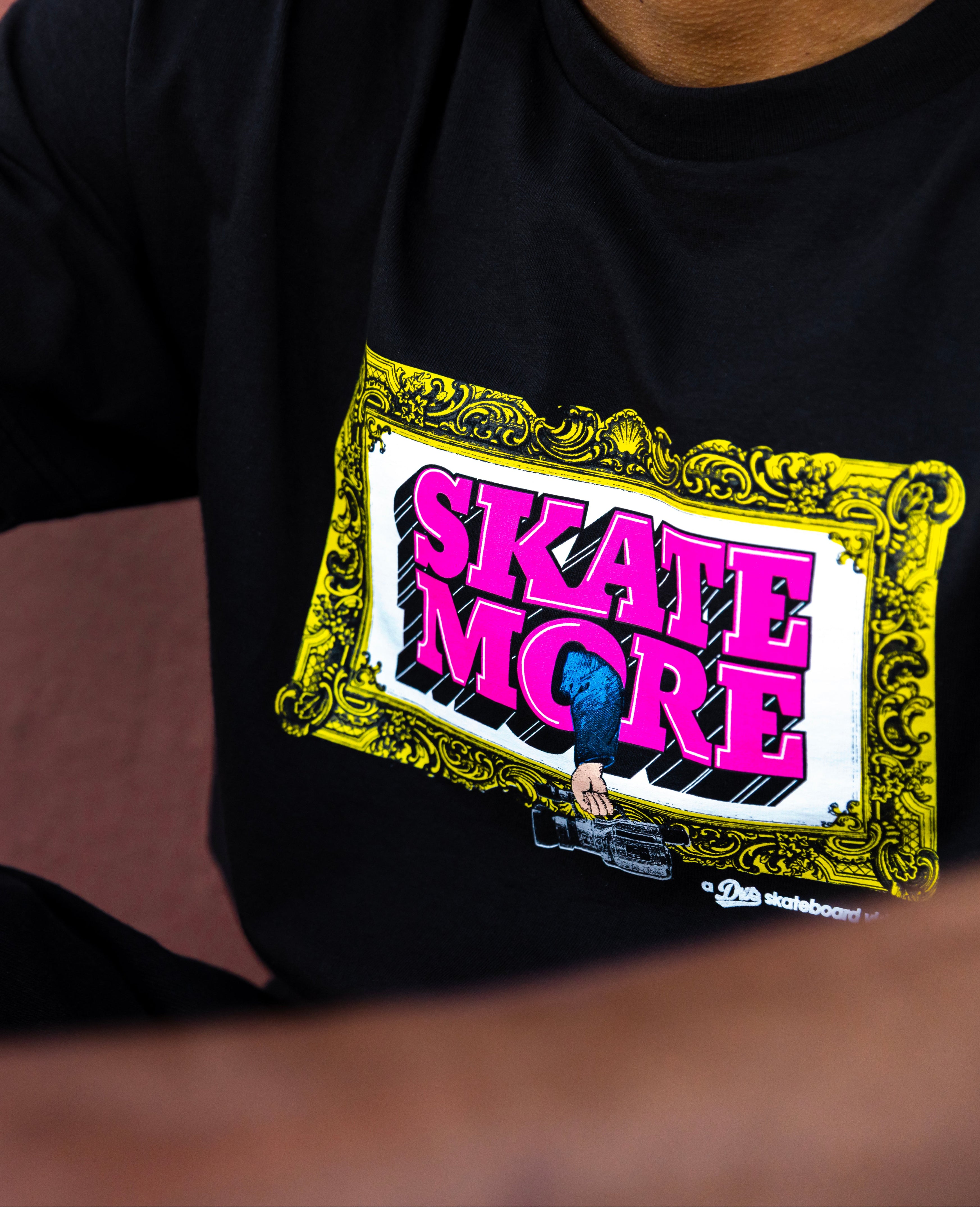 Black t-shirt with 'SKATE MORE' graphic design on a blurred background