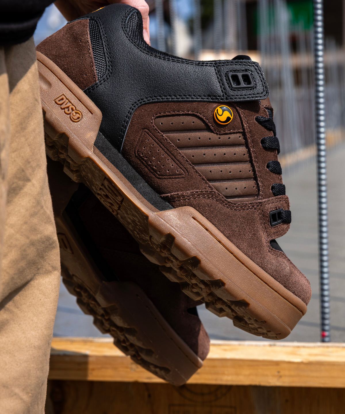 Brown and black shoe with a visible brand logo held by a person outdoors.