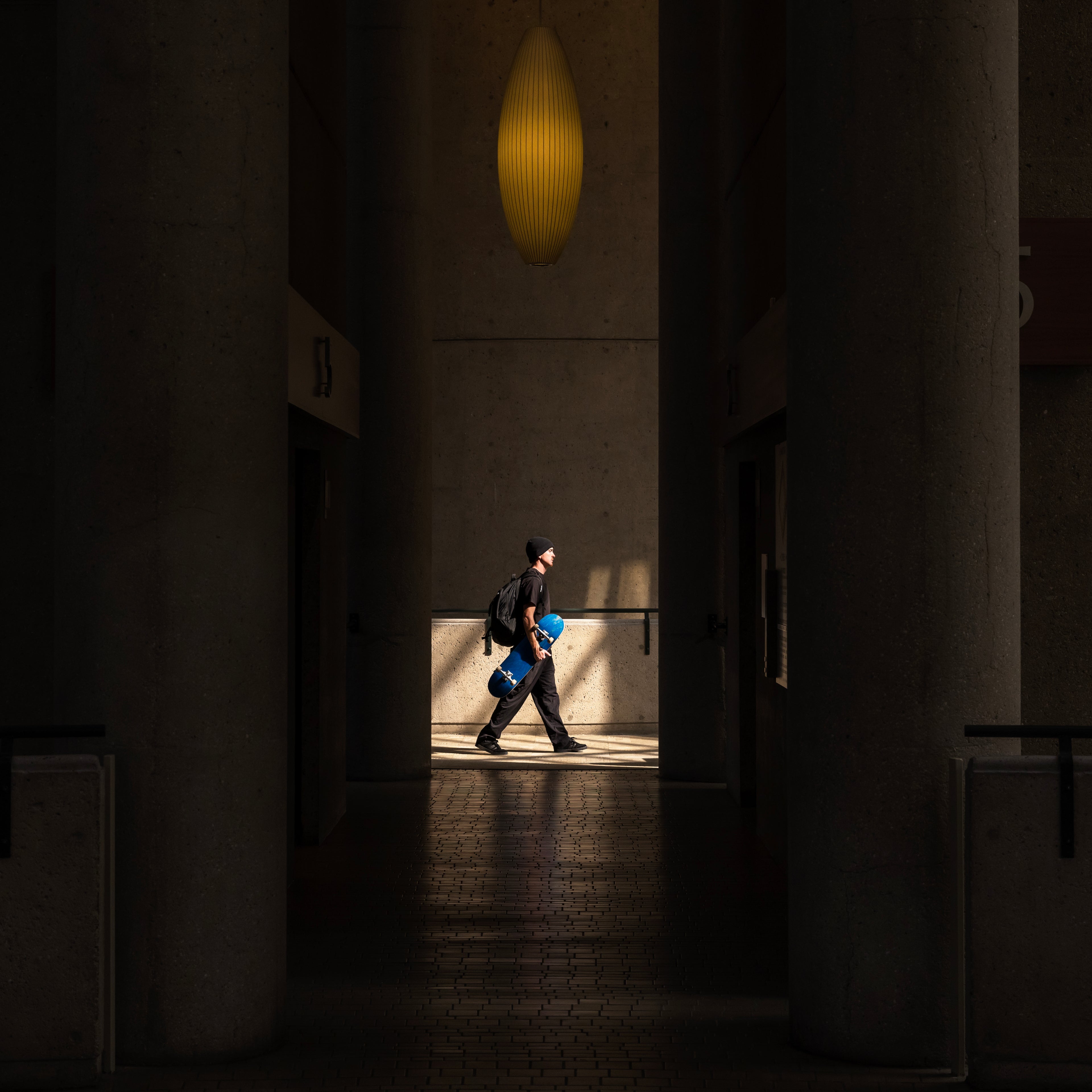 Person walking through a dimly lit hallway with a light fixture above