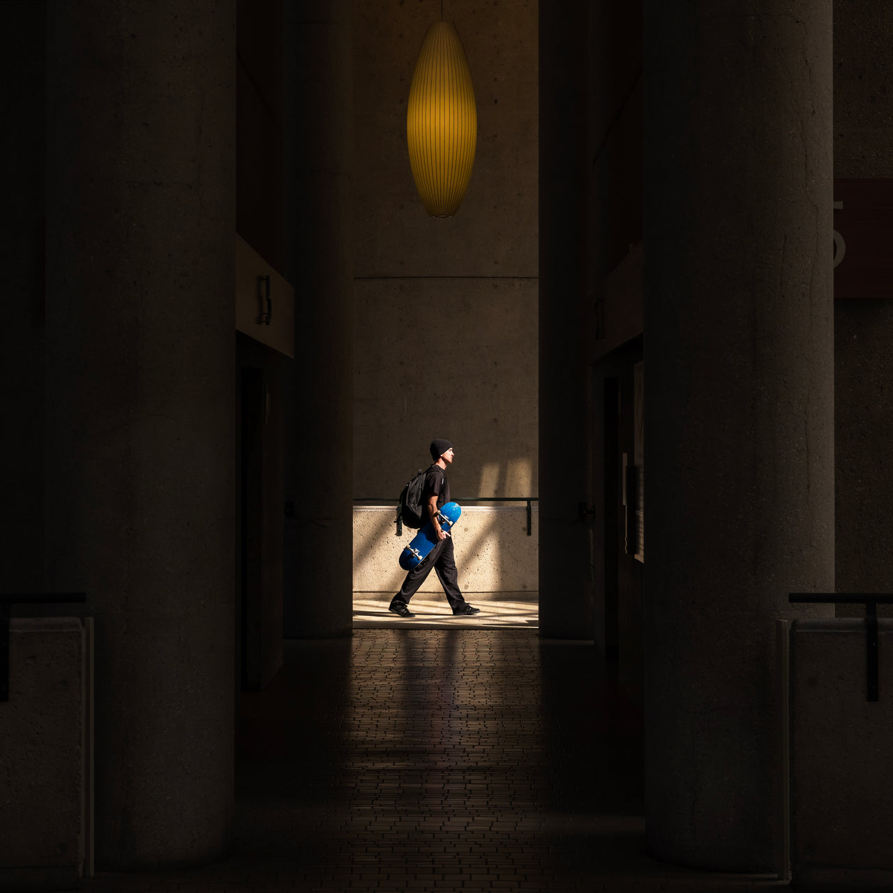 Person walking through a dimly lit hallway with a light fixture above